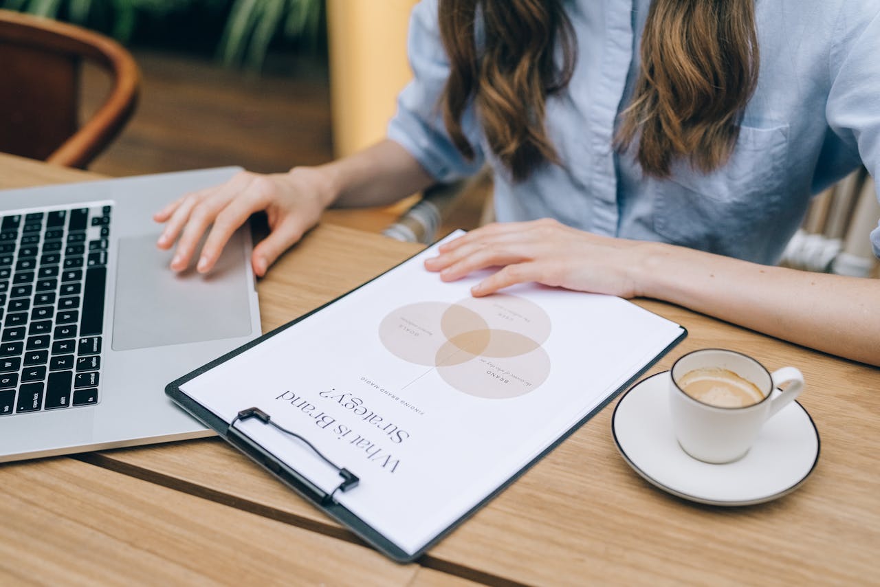 A person reviews a brand strategy document on a clipboard while using a laptop in an office setting.